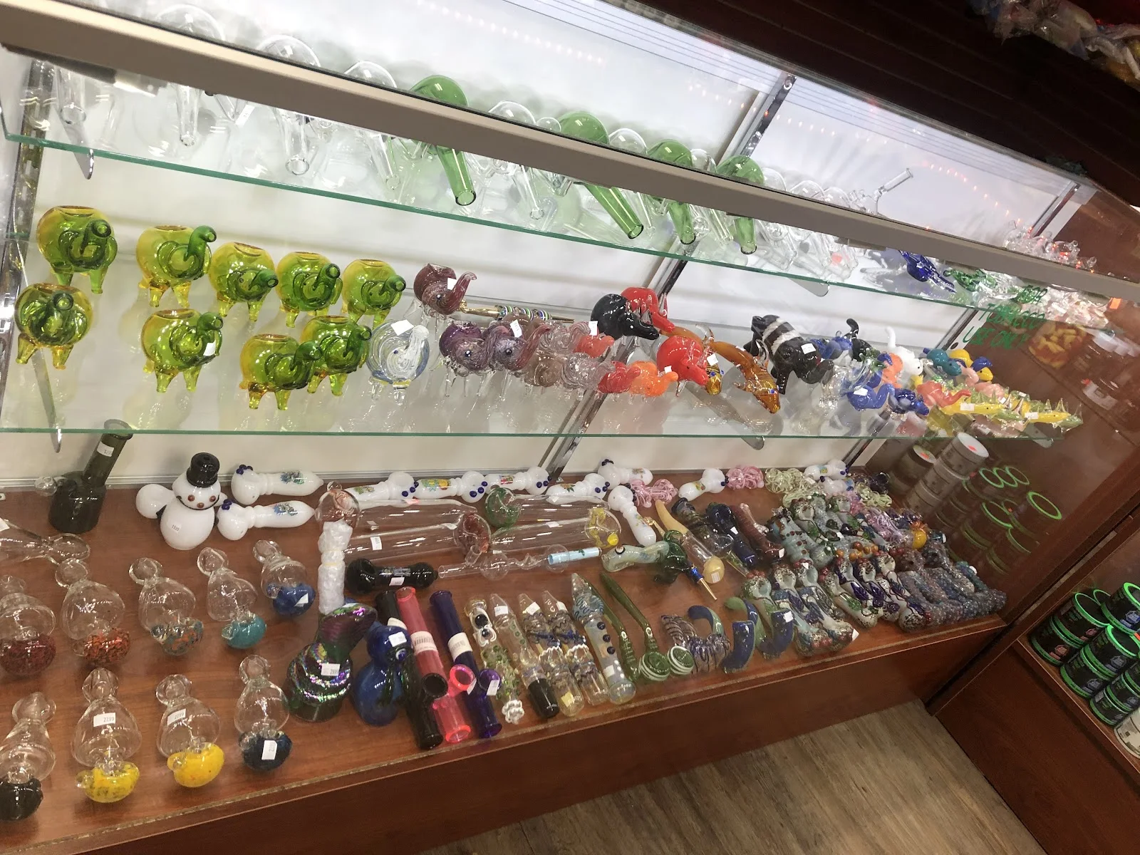 Counter case of coloured glass hand pipes, chillums and animal-shaped pipes